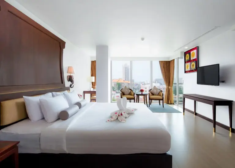 Kingsize-Schlafzimmer im Aiyara Grand Hotel Pattaya mit herzförmigen Handtuchschwänen und klassischem Holz-Kopfteil