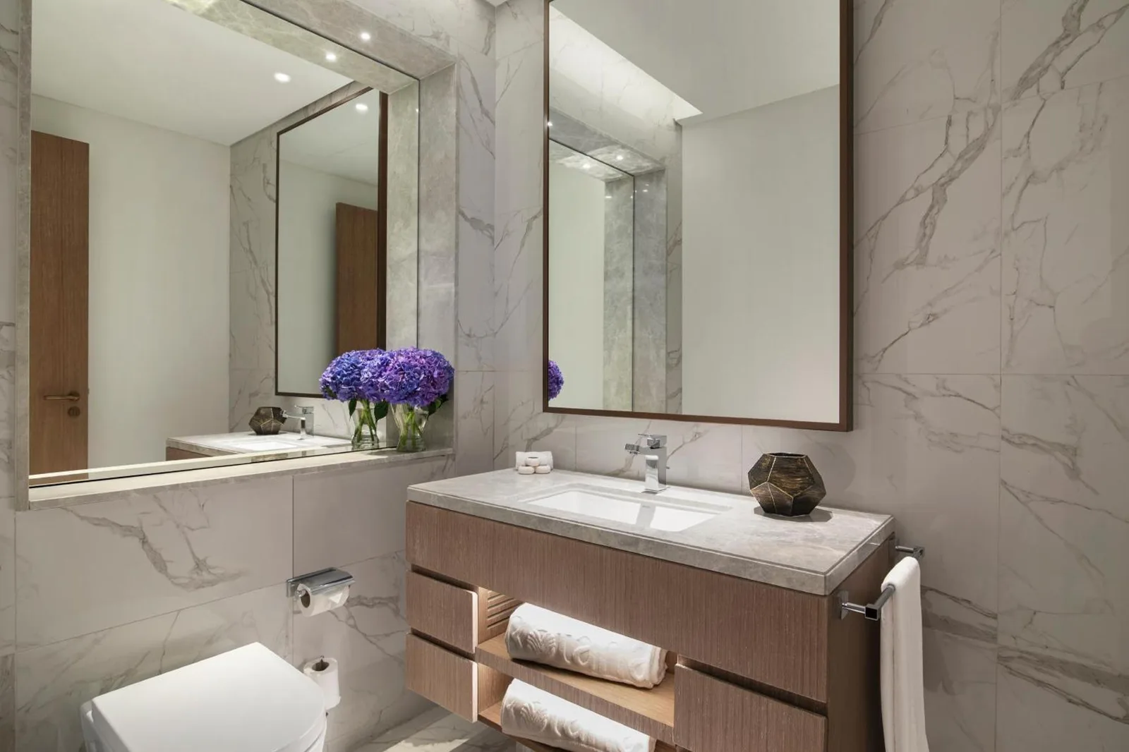 Al Jaddaf Rotana Dubai bathroom vanity with marble walls, mirror, and neatly arranged amenities