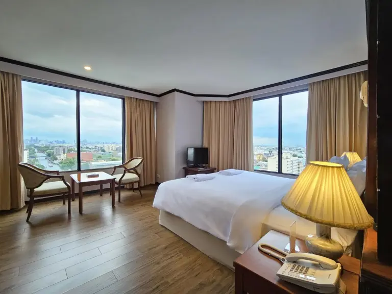 Chambre d’angle du Alexander Hotel Bangkok avec grandes fenêtres, vue sur la ville et lit king size