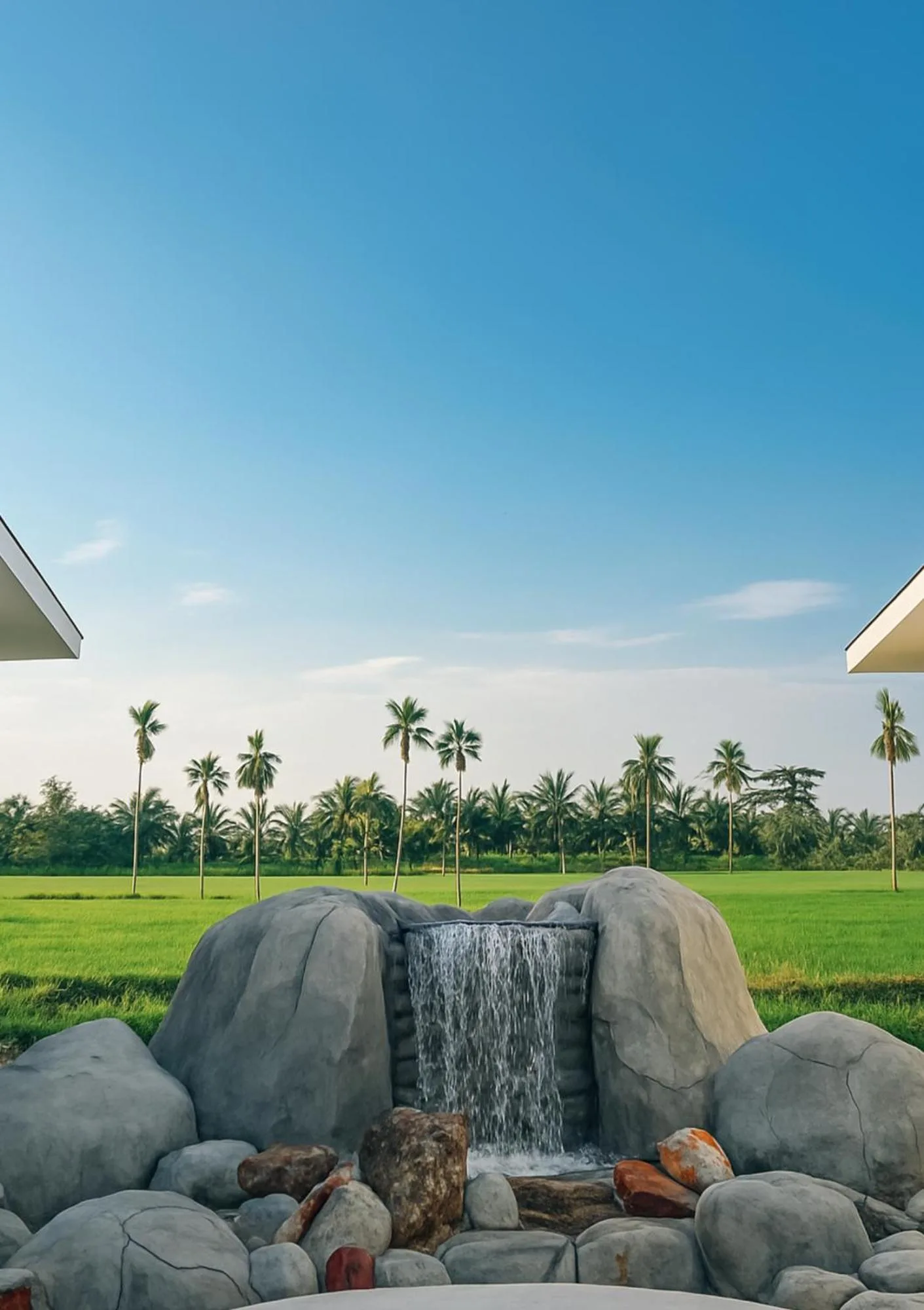 Scenic garden waterfall view at Amal Zone Villa in Pontianak with palm trees and open green landscape.