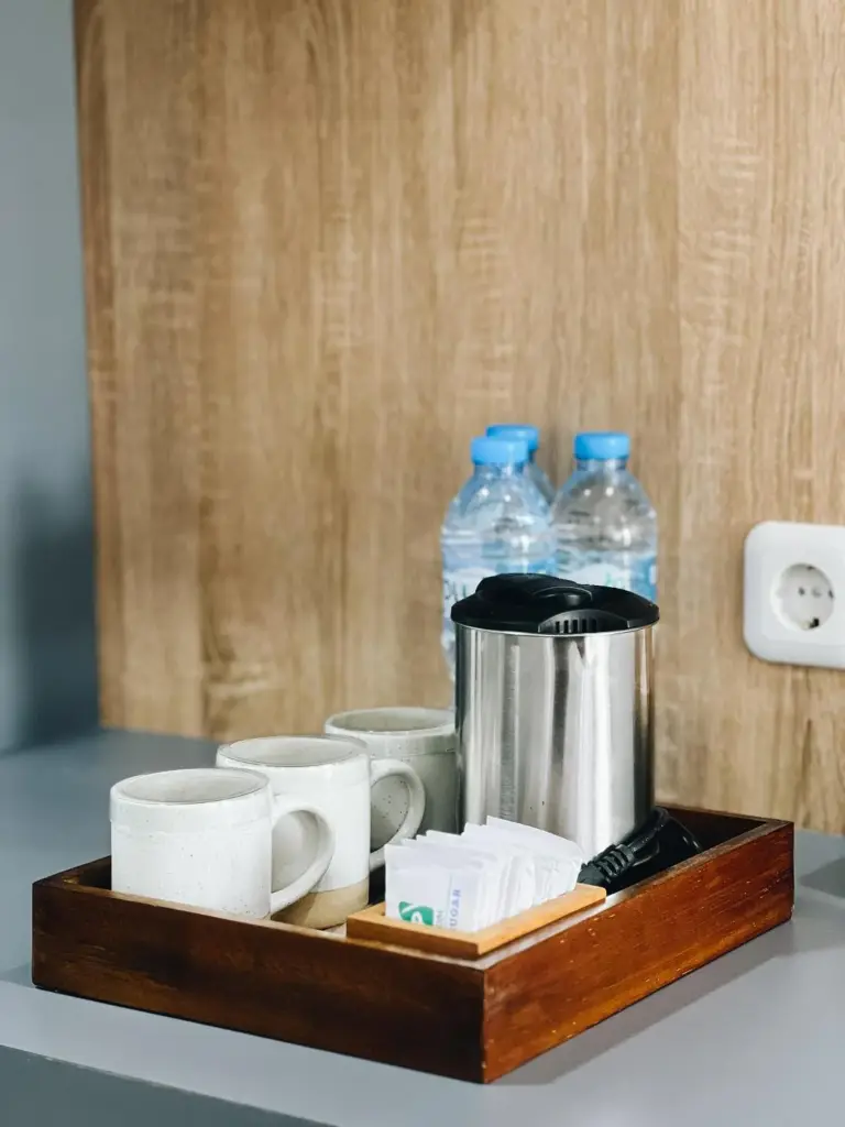In-room tea and coffee tray at Amal Zone Villa Pontianak with cups, water bottles, and kettle.