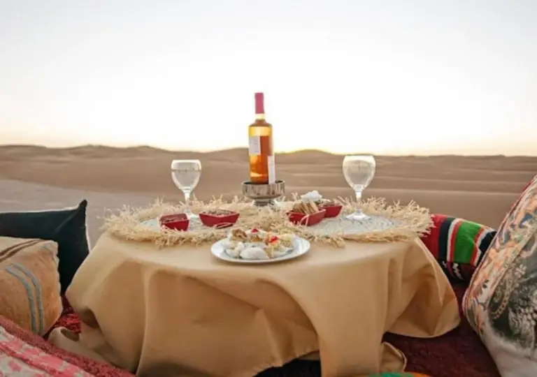 Mesa privada para cenar en el desierto en Amazing Luxury Camp en Merzouga con vino, copas y vistas a las dunas
