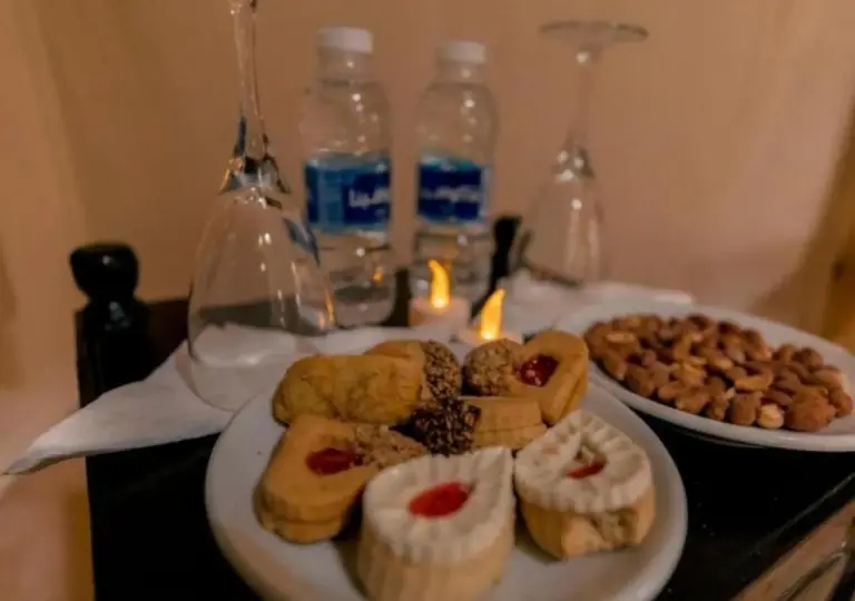 Mesa de postres y aperitivos en Amazing Luxury Camp en Merzouga con vasos de té, pasteles y agua embotellada