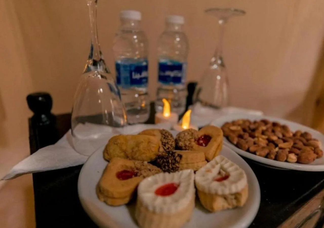 Mesa de postres y aperitivos en Amazing Luxury Camp en Merzouga con vasos de té, pasteles y agua embotellada