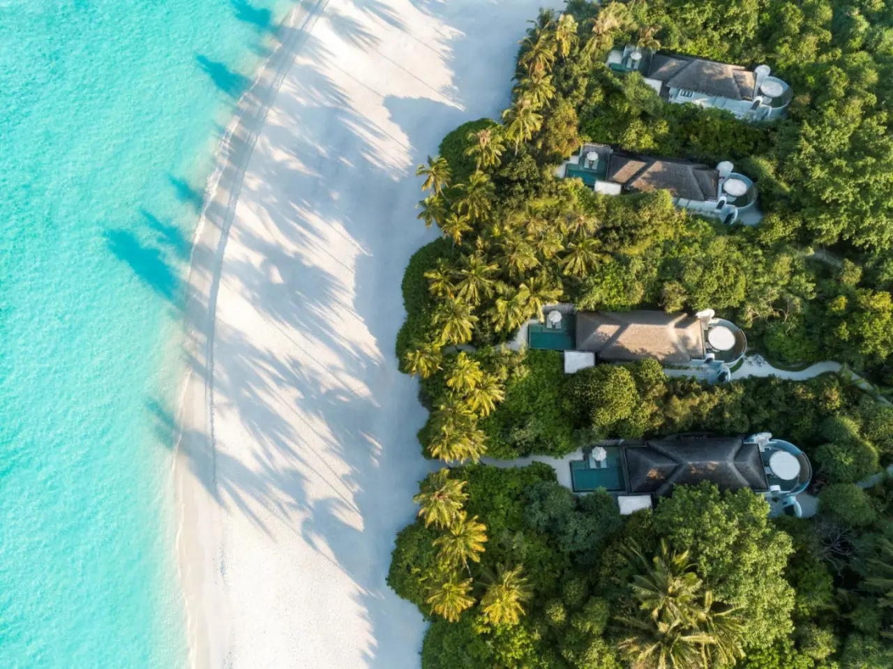 Aerial view of beachside villas at Anantara Kihavah Maldives Villas amidst lush greenery.