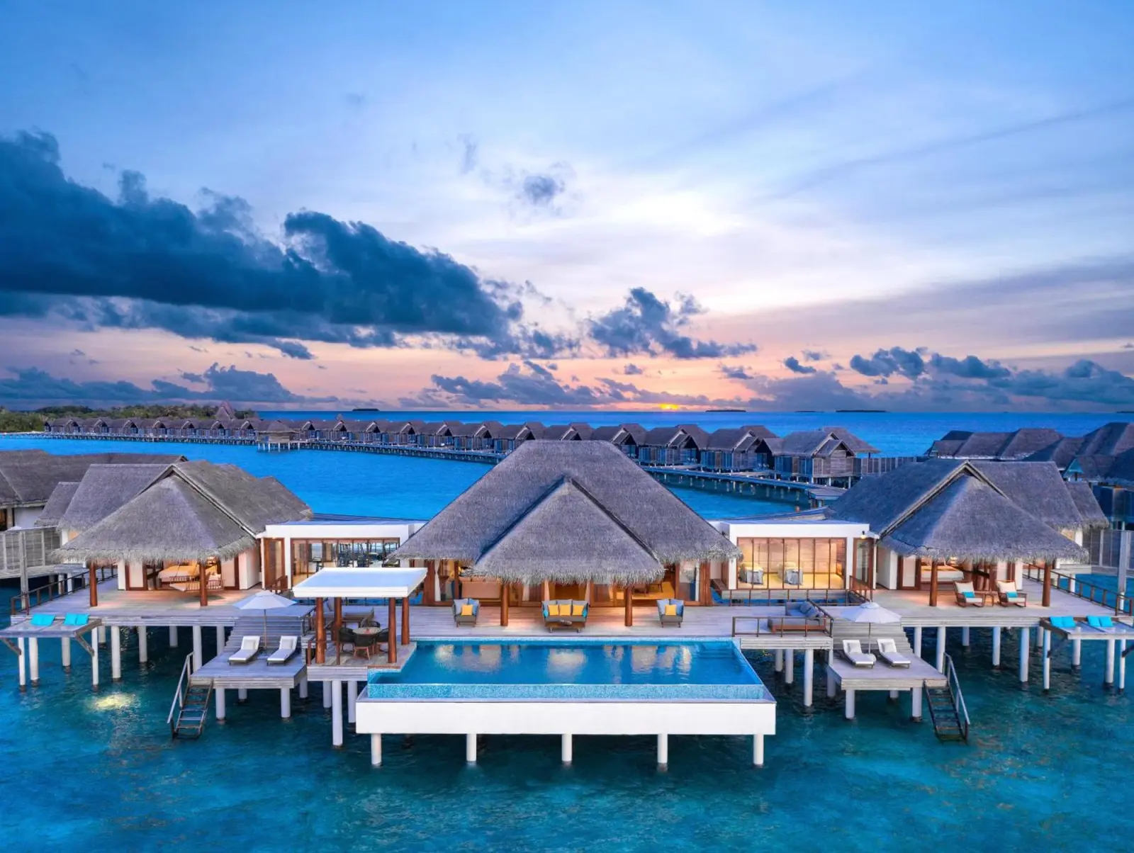 Sunset view over water villas at Anantara Kihavah Maldives Villas with vibrant colors.