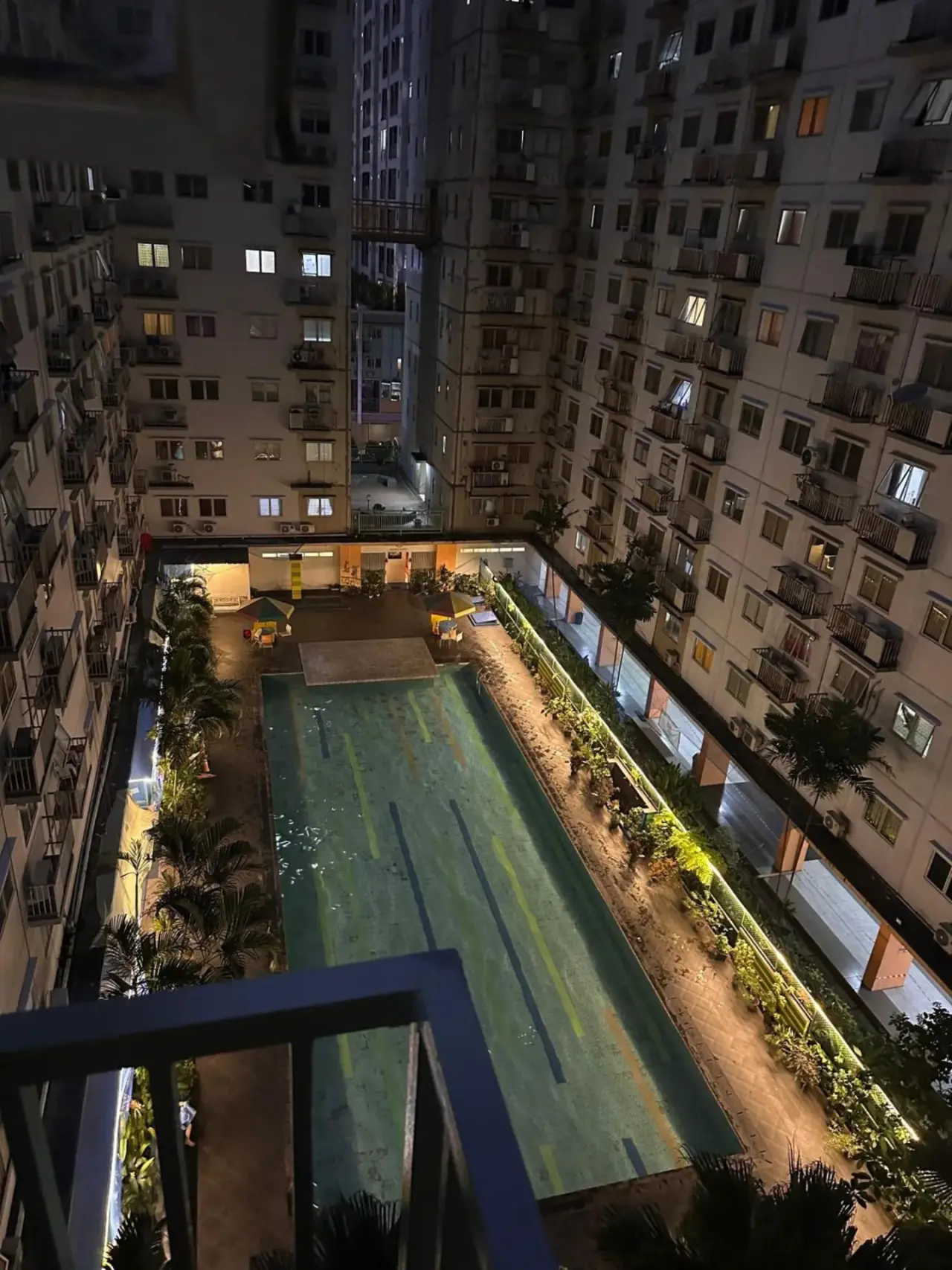 Vue nocturne de la piscine à Apartemen Cantik 2BR-7 orang Kelapa Gading WIFI à Jakarta avec tours d’appartements éclairées et cour intérieure.