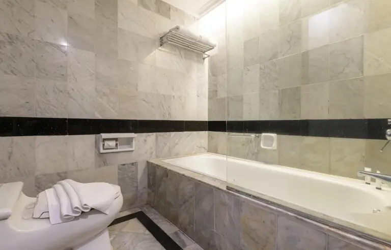 Marble bathroom at ARTOTEL Suites Aquila Bandung with bathtub, toilet, and glass shower partition