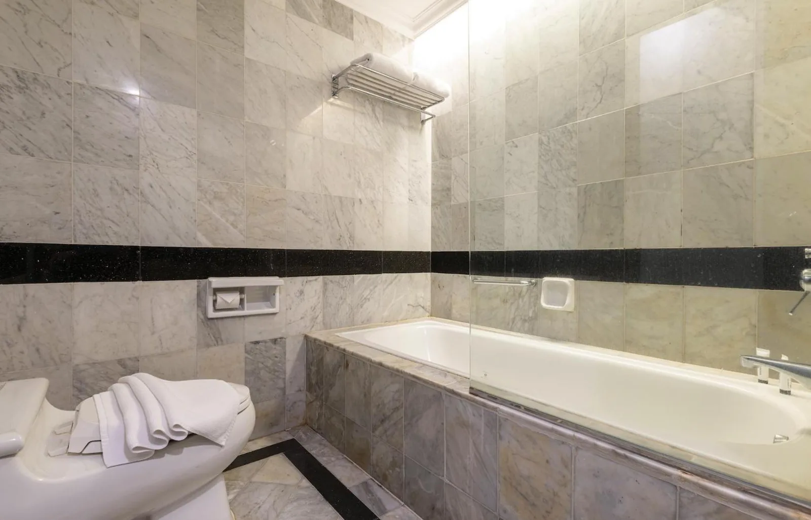 Marble bathroom at ARTOTEL Suites Aquila Bandung with bathtub, toilet, and glass shower partition