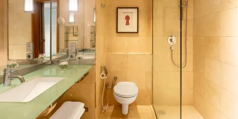 Salle de bains de Aryaduta Menteng à Jakarta avec douche vitrée, lavabo et toilettes dans une finition en pierre.