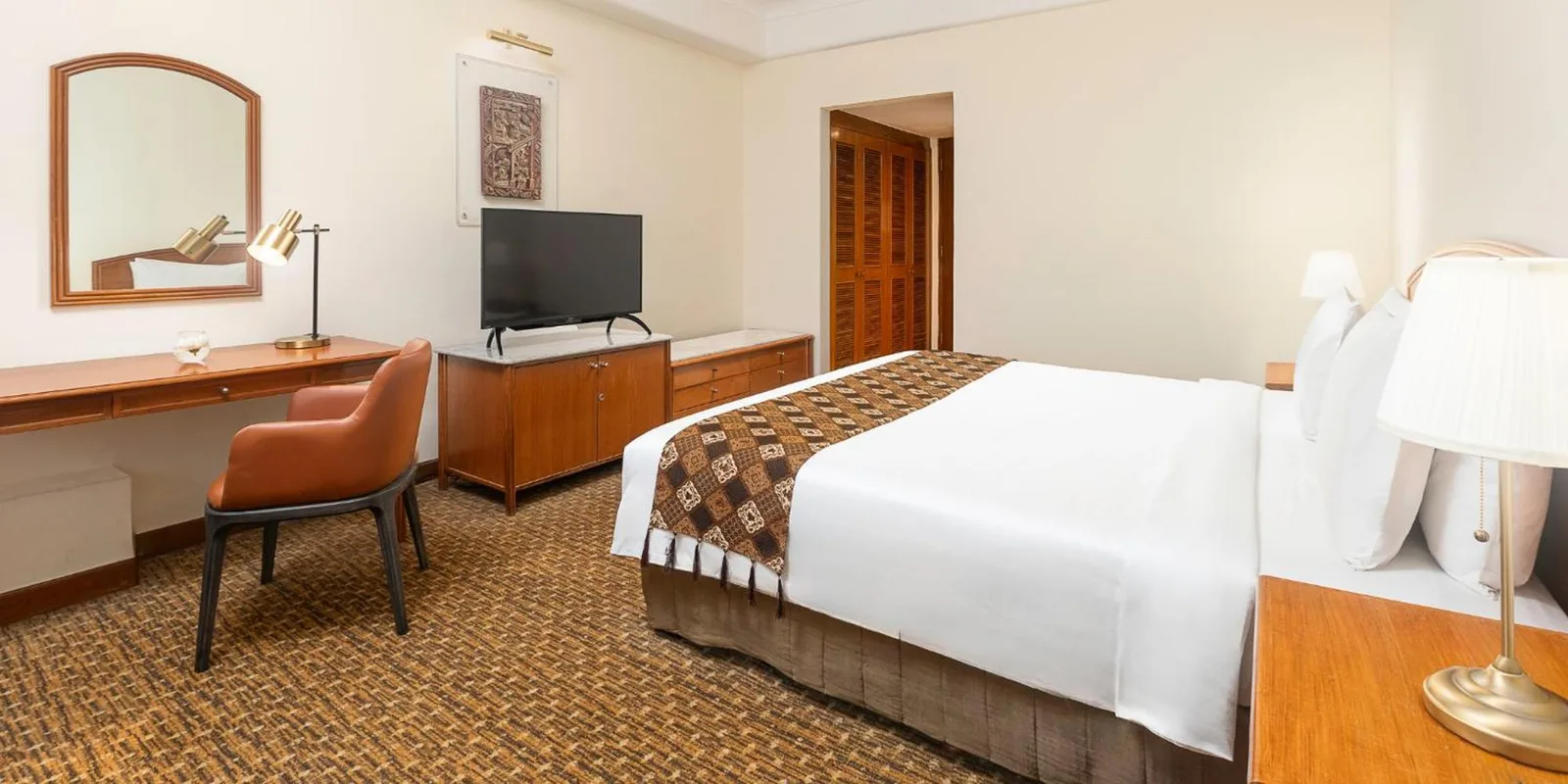Chambre d’hôtes de Aryaduta Menteng à Jakarta avec un lit king size, un bureau, un coin salon et une grande fenêtre.