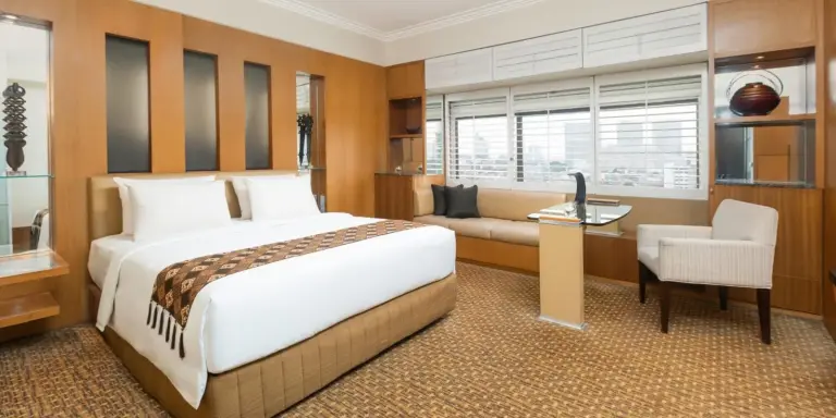 Chambre suite de Aryaduta Menteng à Jakarta avec lit king size, coin salon, bureau et fenêtre avec vue sur la ville.