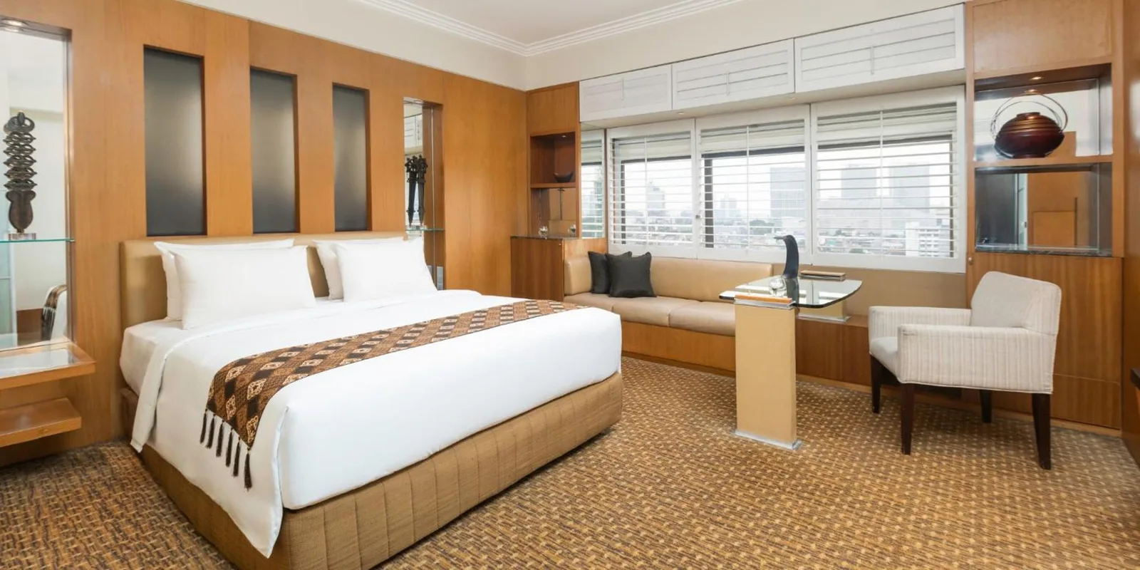 Chambre suite de Aryaduta Menteng à Jakarta avec lit king size, coin salon, bureau et fenêtre avec vue sur la ville.