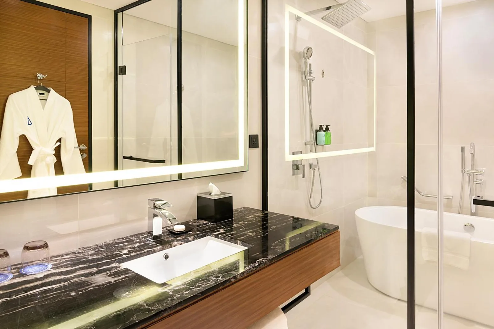 Asiana Grand Hotel Dubai Badezimmer mit Marmorwaschtisch, beleuchtetem Spiegel, Glasdusche und Badewanne