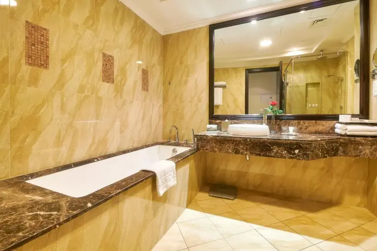 Salle de bains luxueuse au Bahi Ajman Palace Hotel à Ajman avec baignoire, meuble-vasque en marbre et miroir