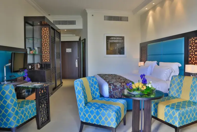 Chambre deluxe au Bahi Ajman Palace Hotel à Ajman avec fauteuils à motifs, bureau et lit king-size