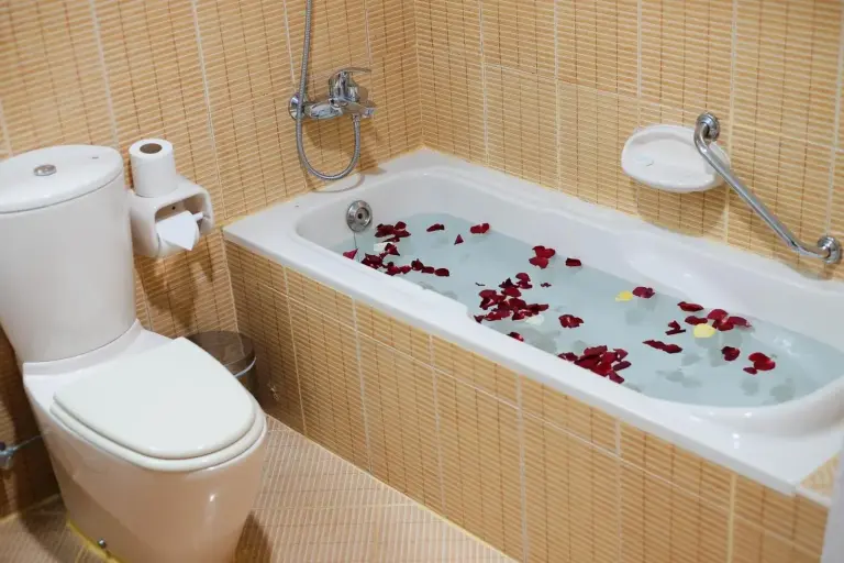 Bathroom at Baity Hotel Apartments in Dubai with bathtub, toilet, and rose petals in the bath.