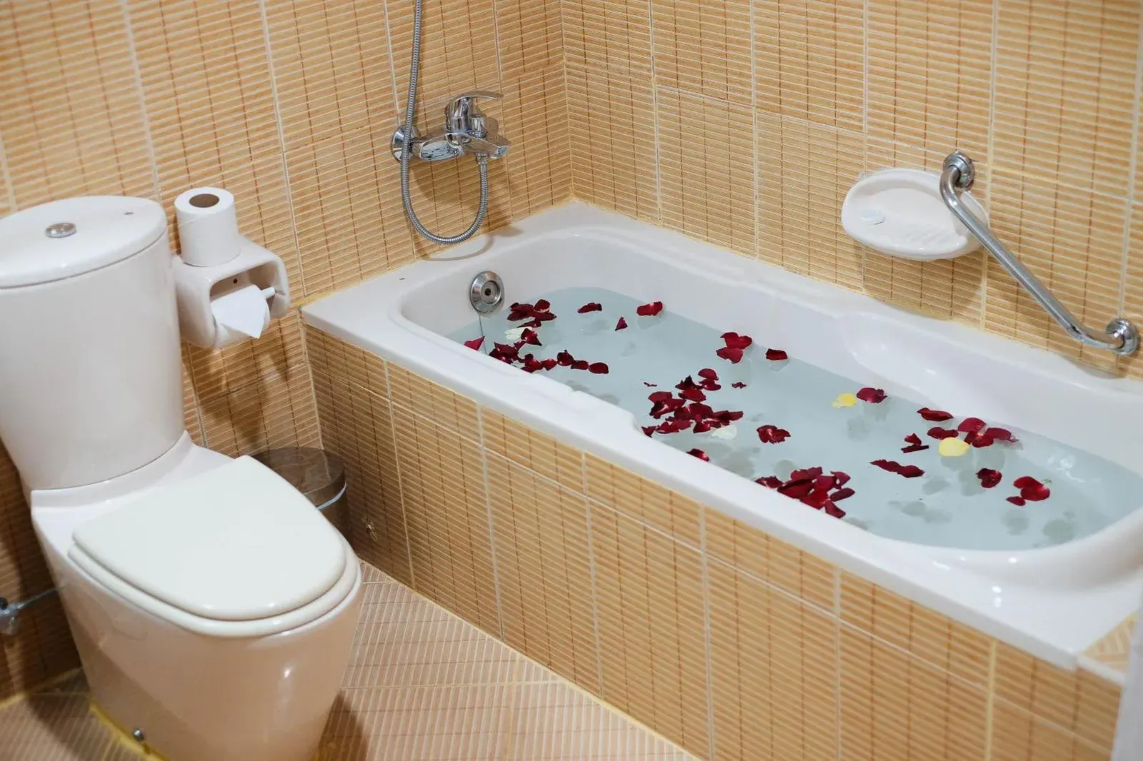 Bathroom at Baity Hotel Apartments in Dubai with bathtub, toilet, and rose petals in the bath.