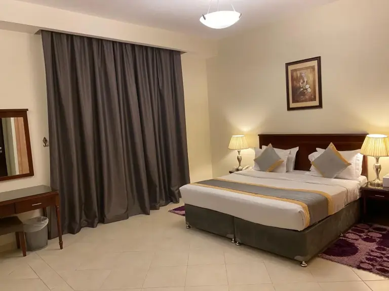 Bright bedroom at Baity Hotel Apartments in Dubai with double bed, curtains, mirror, and dressing table.