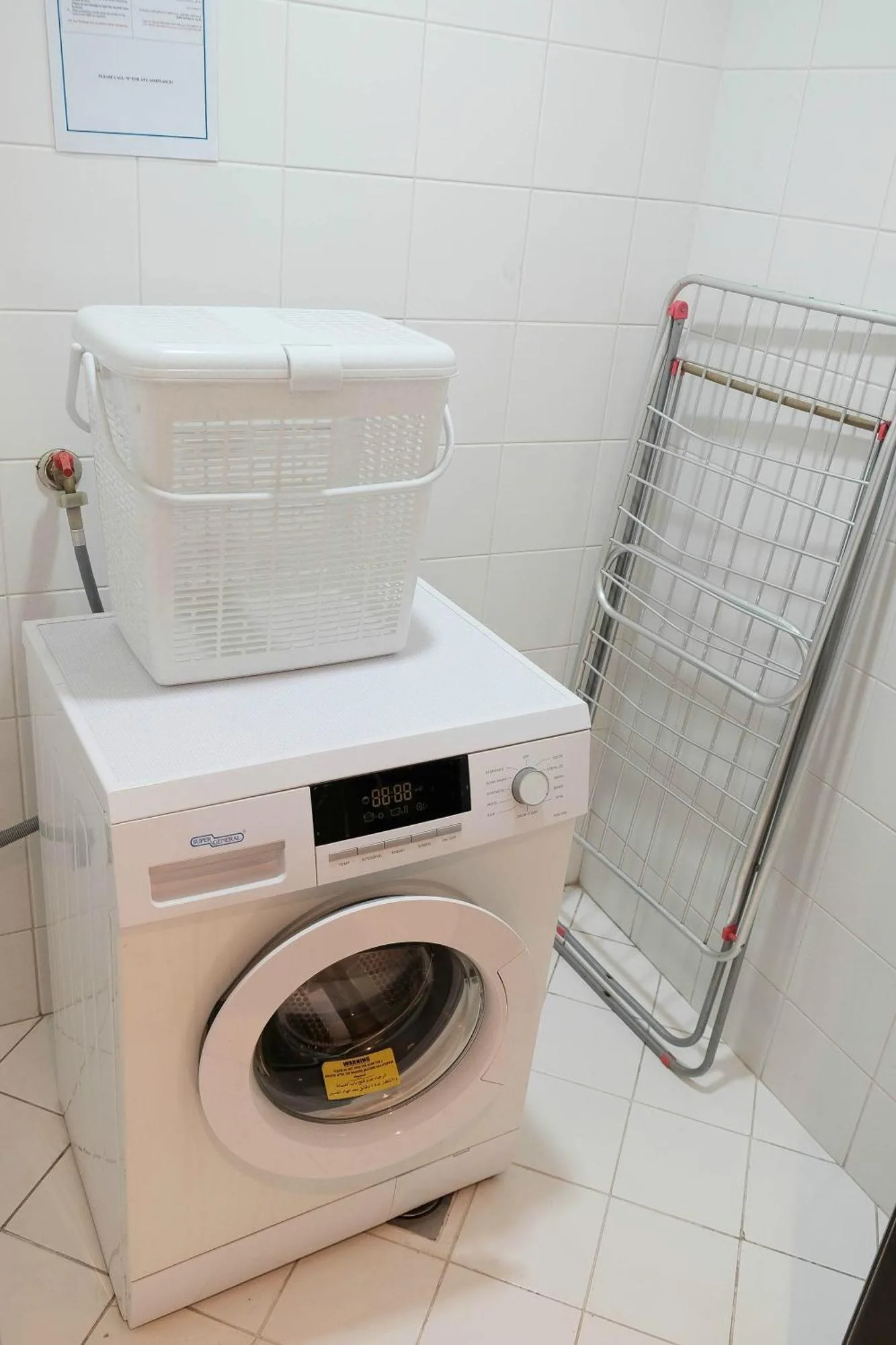 Laundry area at Baity Hotel Apartments in Dubai with washing machine and drying rack.