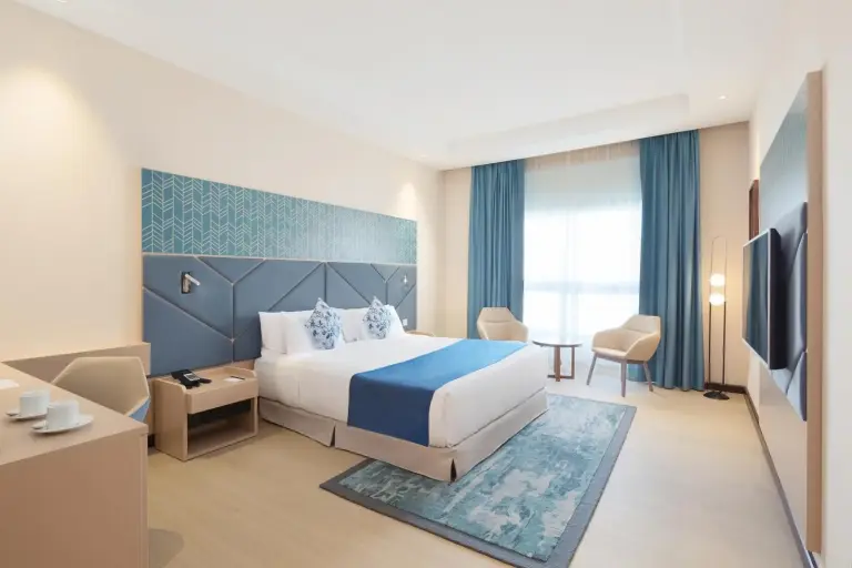 Twin-Gästezimmer im Barcelo Al Jaddaf, Dubai mit großem Fenster, blauen Vorhängen und Stadt-Skyline
