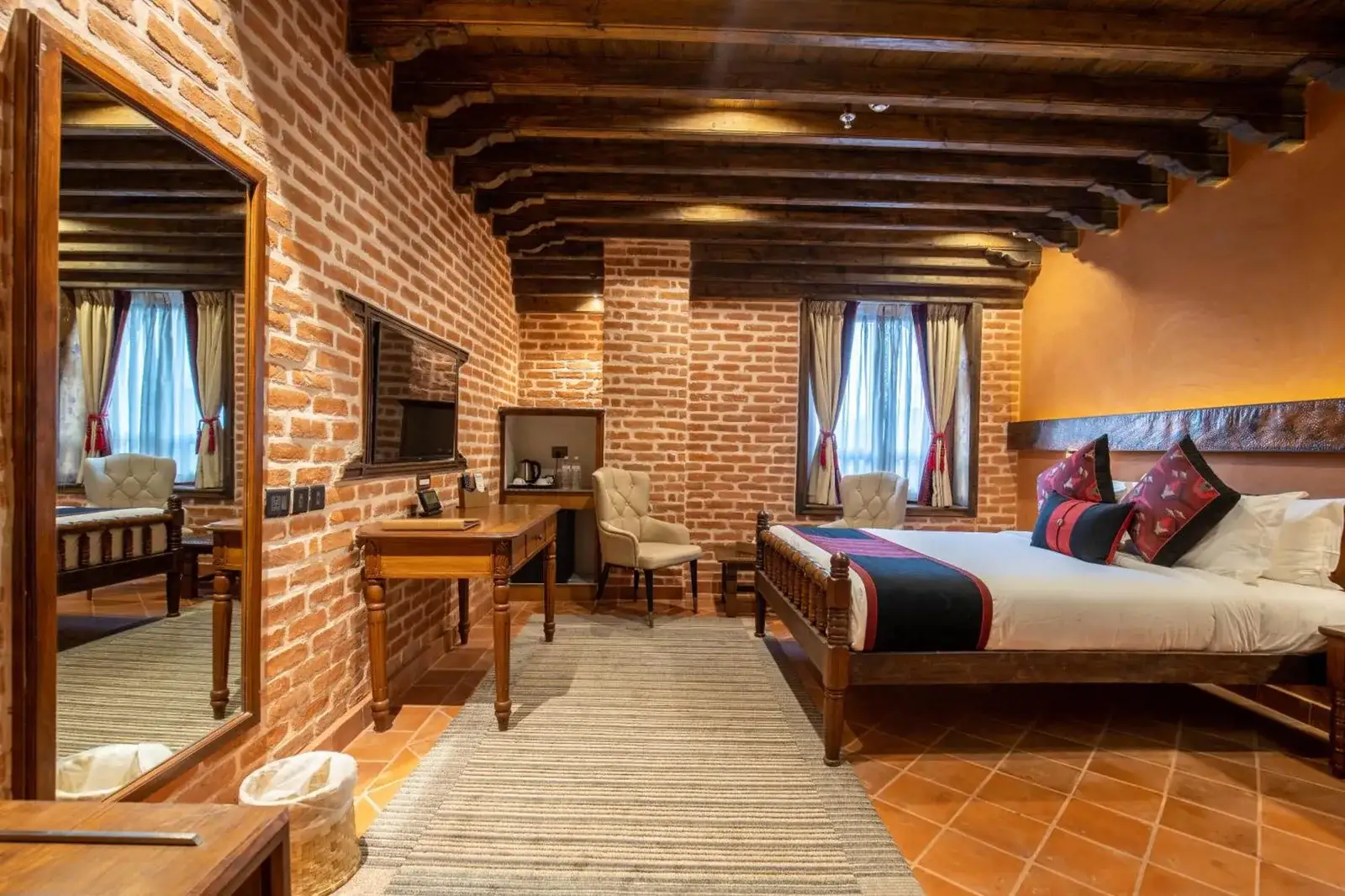 Una elegante habitación de huéspedes con detalles de ladrillo en Basera Boutique Hotel - La escapada oculta de Kathmandu, con una cama king y vigas de madera en el techo.