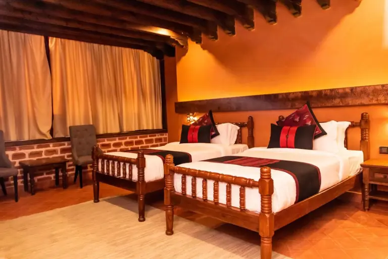Una habitación con dos camas en Basera Boutique Hotel - La escapada oculta de Kathmandu, con muebles de madera tradicionales y acogedoras paredes naranjas.
