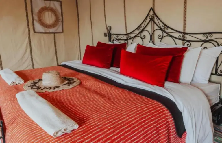 Neatly prepared double bed at Bedouin Desert Camp in Merzouga with red bedding and decorative pillows