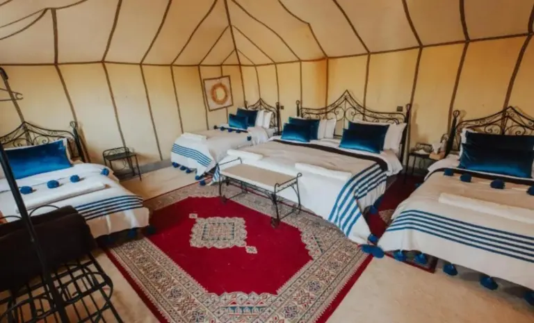 Spacious family tent room at Bedouin Desert Camp in Merzouga with multiple beds, a red rug, and blue cushions