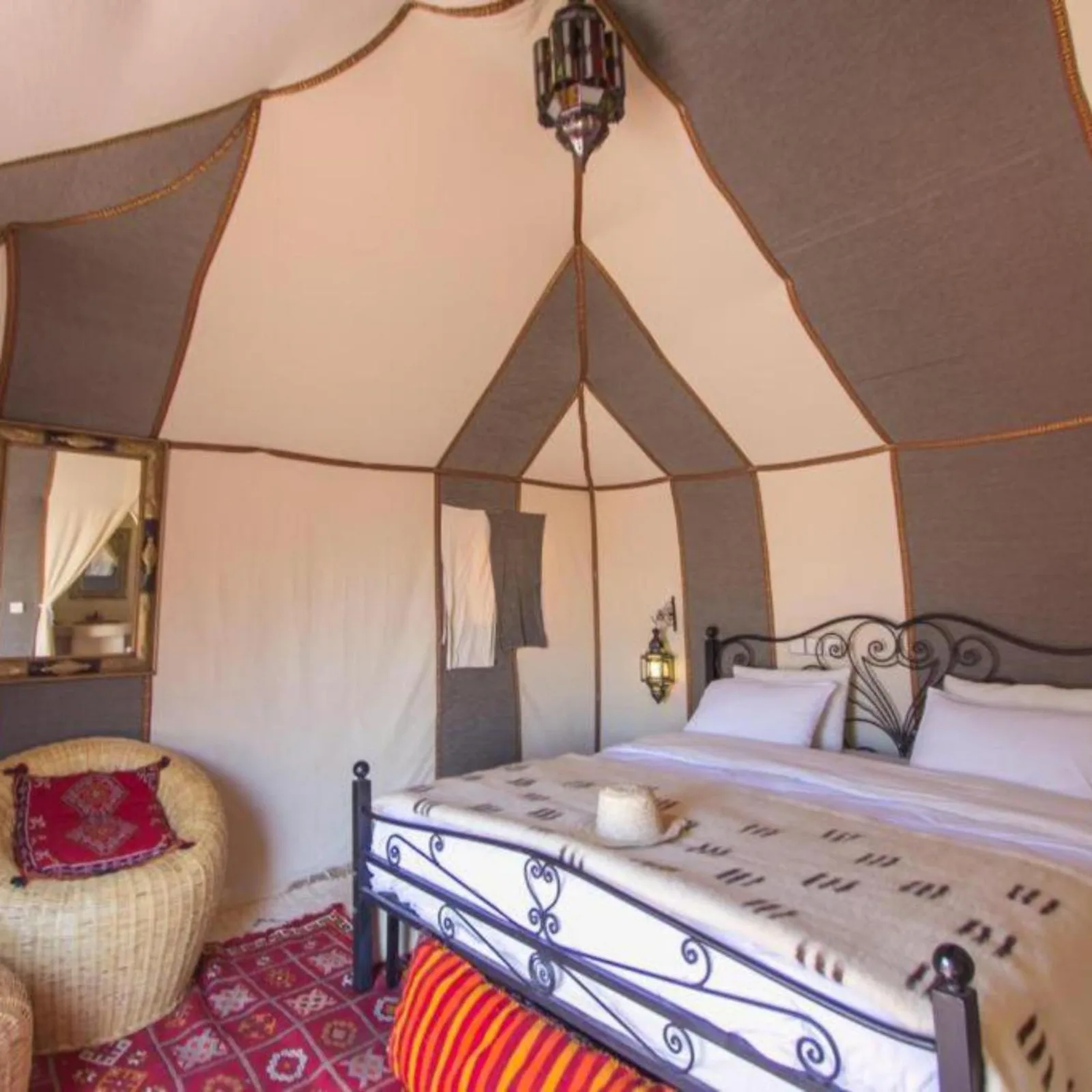 Geräumige Zelt-Suite im Berber Soul luxury Camp in Merzouga mit schmiedeeisernem Bett, geflochtenem Stuhl und gemustertem Teppich