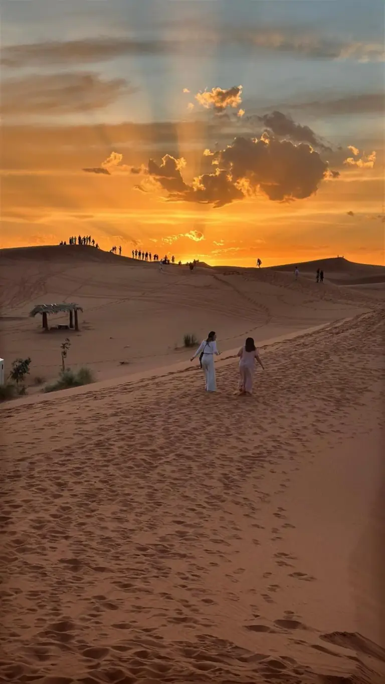Coucher de soleil sur les dunes de sable près de Berber Spirit Luxury Camp à Merzouga avec des clients traversant le désert.