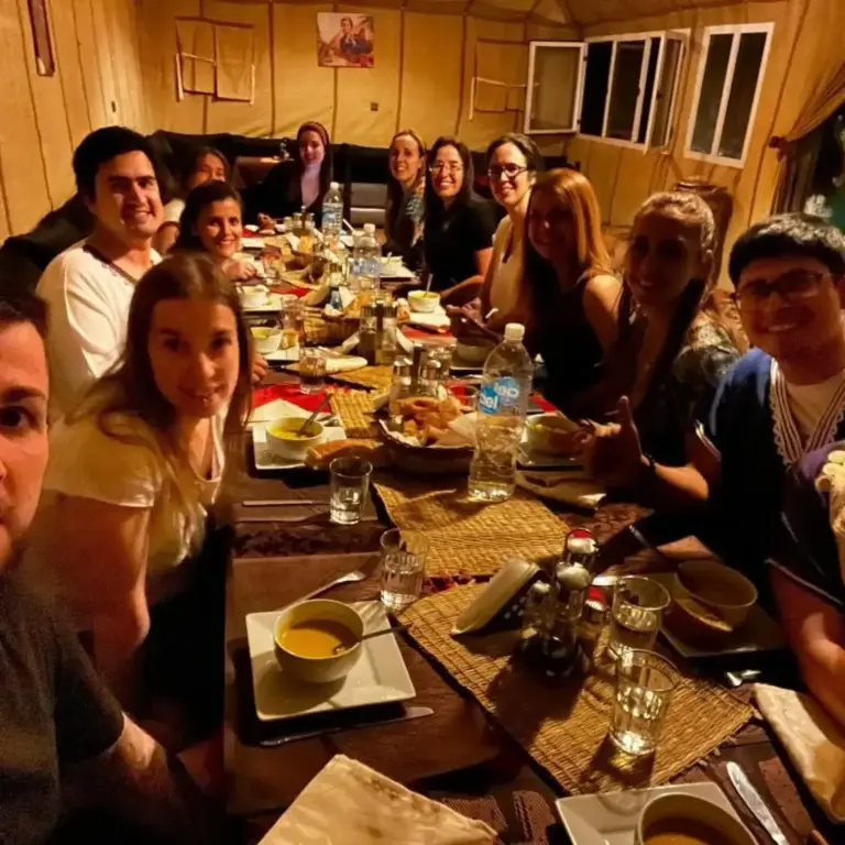 Group dinner inside Bikhir Luxury Camp in Merzouga with guests seated at a shared table