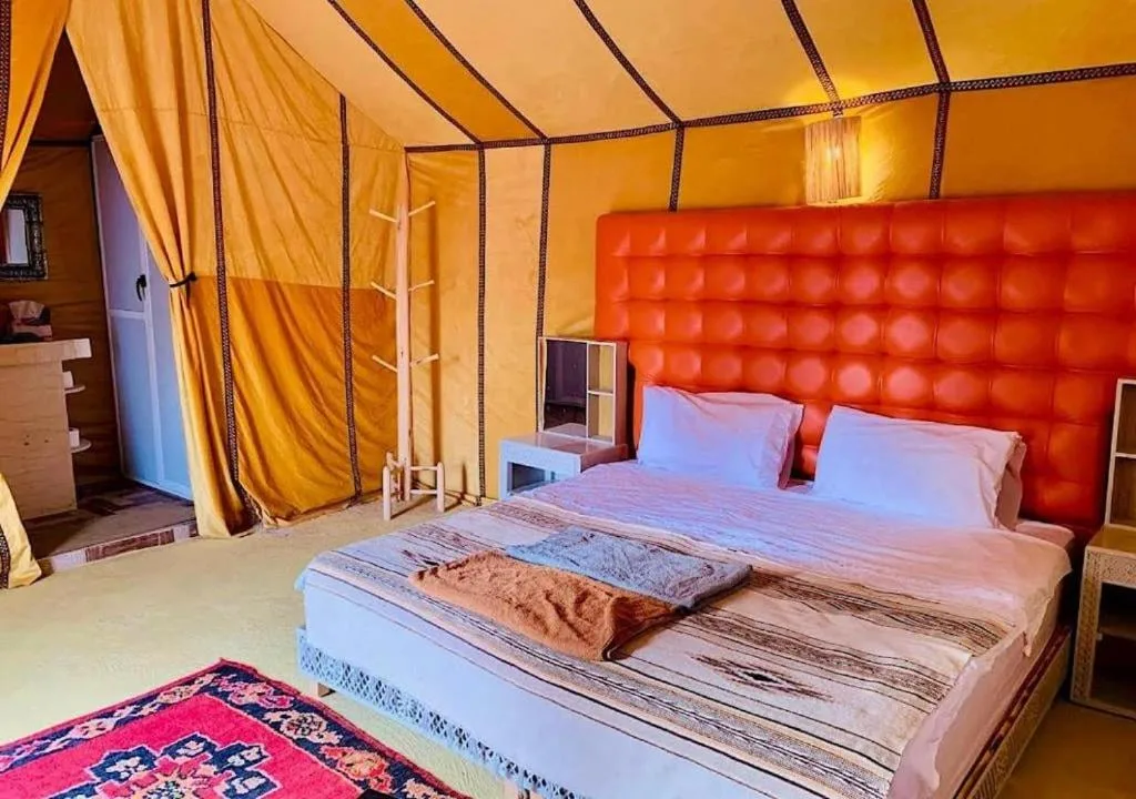 Colorful deluxe tent room at Blue Sky Luxury Camp in Merzouga with an orange headboard and desert lodge atmosphere.