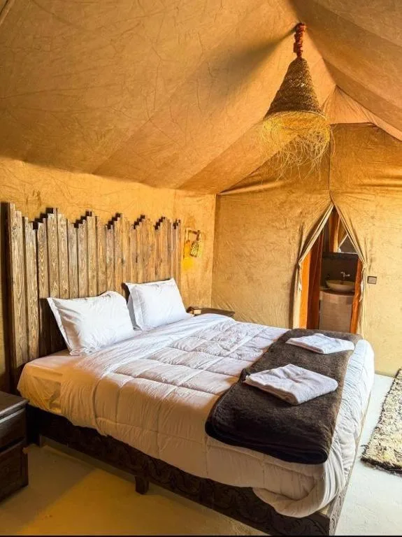 Luxury tent bedroom at Blue Sky Luxury Camp in Merzouga with a large bed, wooden details, and a private bathroom entrance.