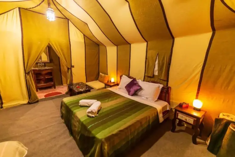 Standard tent bedroom at Blue Sky Luxury Camp in Merzouga with a double bed, bedside lamps, and warm yellow canvas walls.