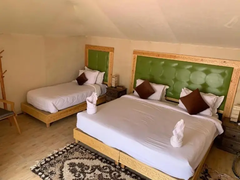 Twin guest room at Blue Sky Luxury Camp in Merzouga featuring two beds, a green tufted headboard, and Moroccan-style decor.