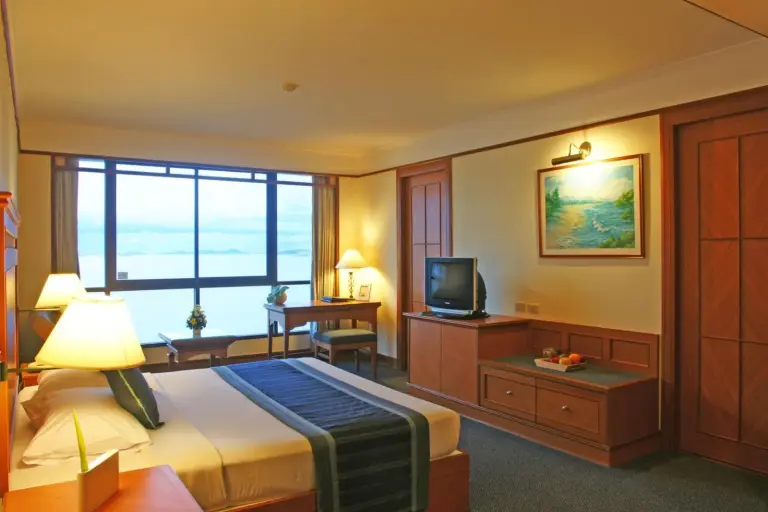 Cholchan Pattaya Beach Resort - SHA Extra Plus Gästezimmer mit Kingsize-Bett und Holzmöbeln in Pattaya