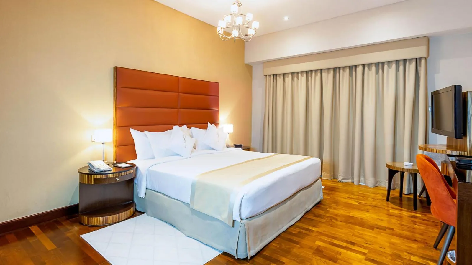 Bedroom at City Premiere Hotel Apartments Dubai with a large bed, bedside lamps, curtains, and work desk.