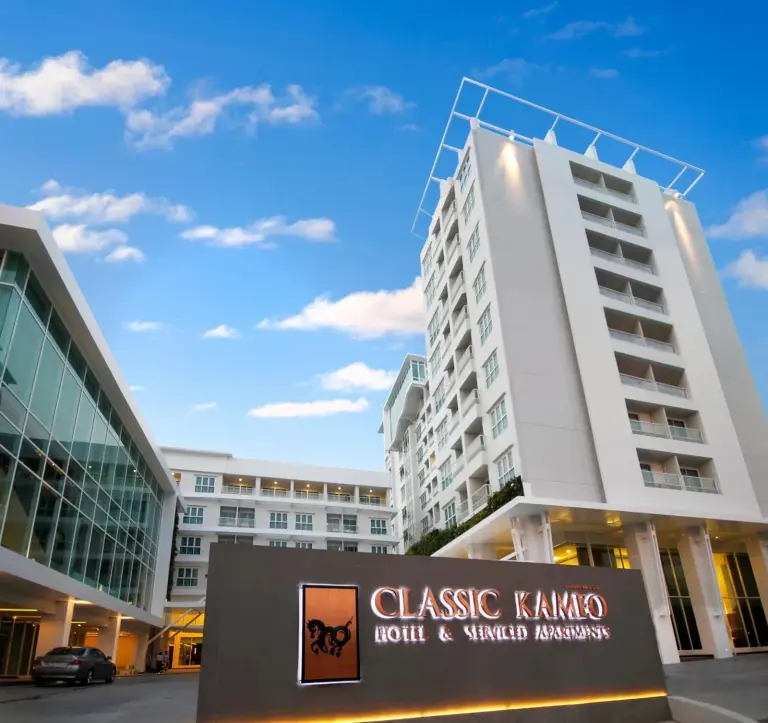 Vue extérieure de Classic Kameo Hotel & Serviced Apartments, Ayutthaya à Ayutthaya avec des tours modernes et une signalétique éclairée.