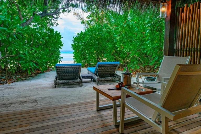 Zone de lounge en bord de mer au Constance Moofushi Maldives avec sièges et végétation.