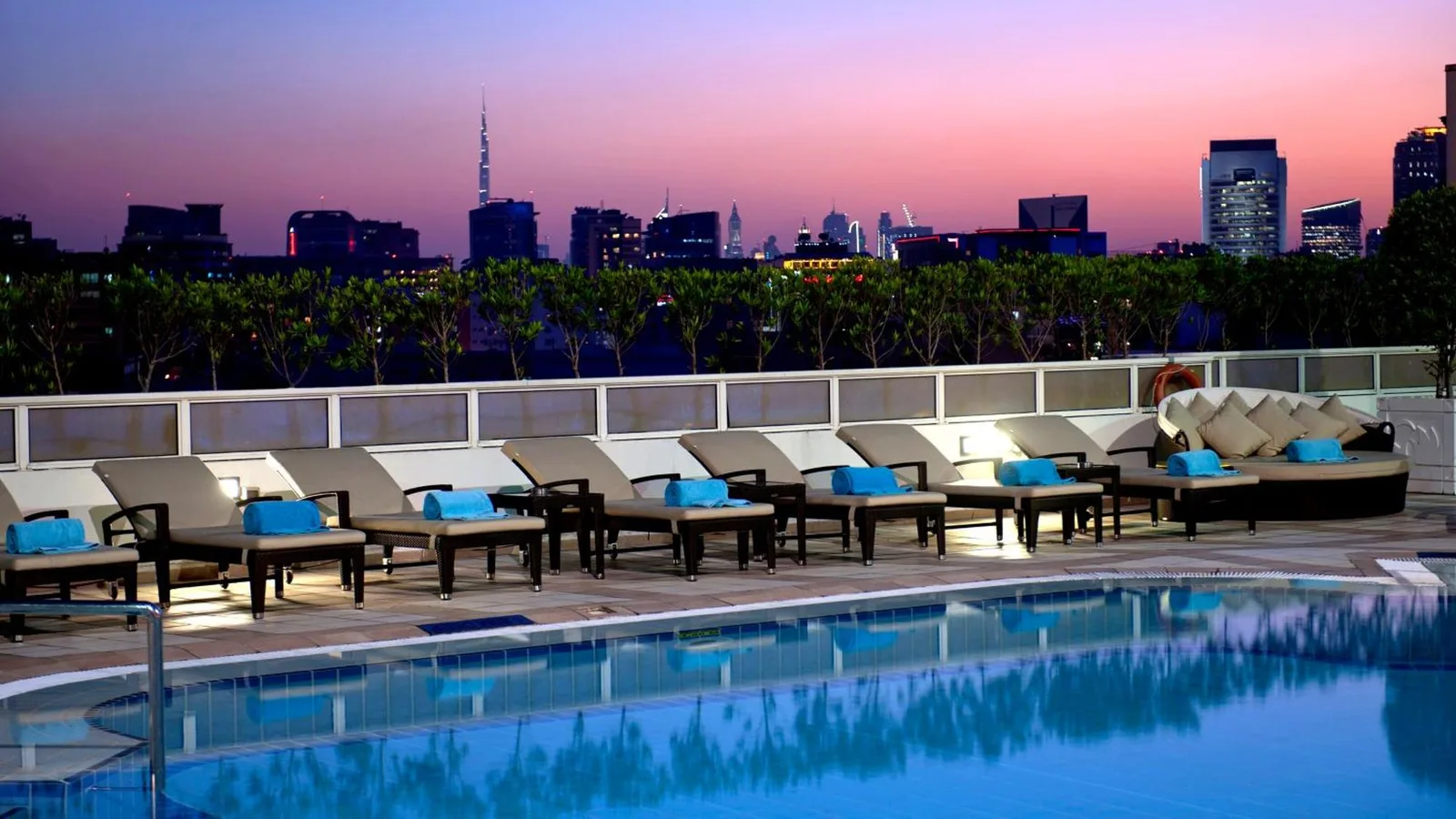 Terrasse de piscine au Crowne Plaza Dubai Deira à Dubai avec chaises longues et skyline de la ville au coucher du soleil