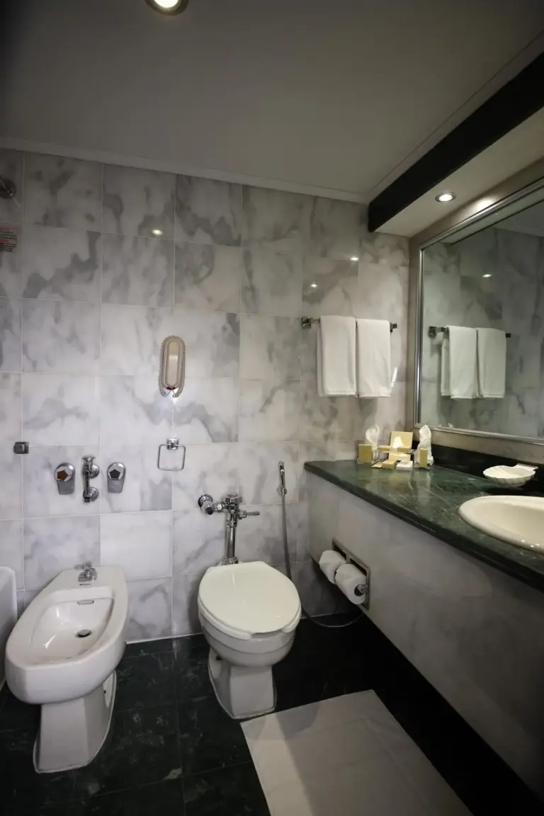 Salle de bains moderne au Danat Al Ain Resort à Al Ain avec murs en marbre, deux lavabos et un bidet.