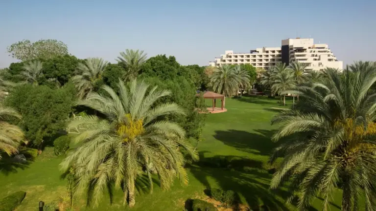 Jardins verdoyants et palmiers au Danat Al Ain Resort à Al Ain avec le bâtiment de l’hôtel au loin.