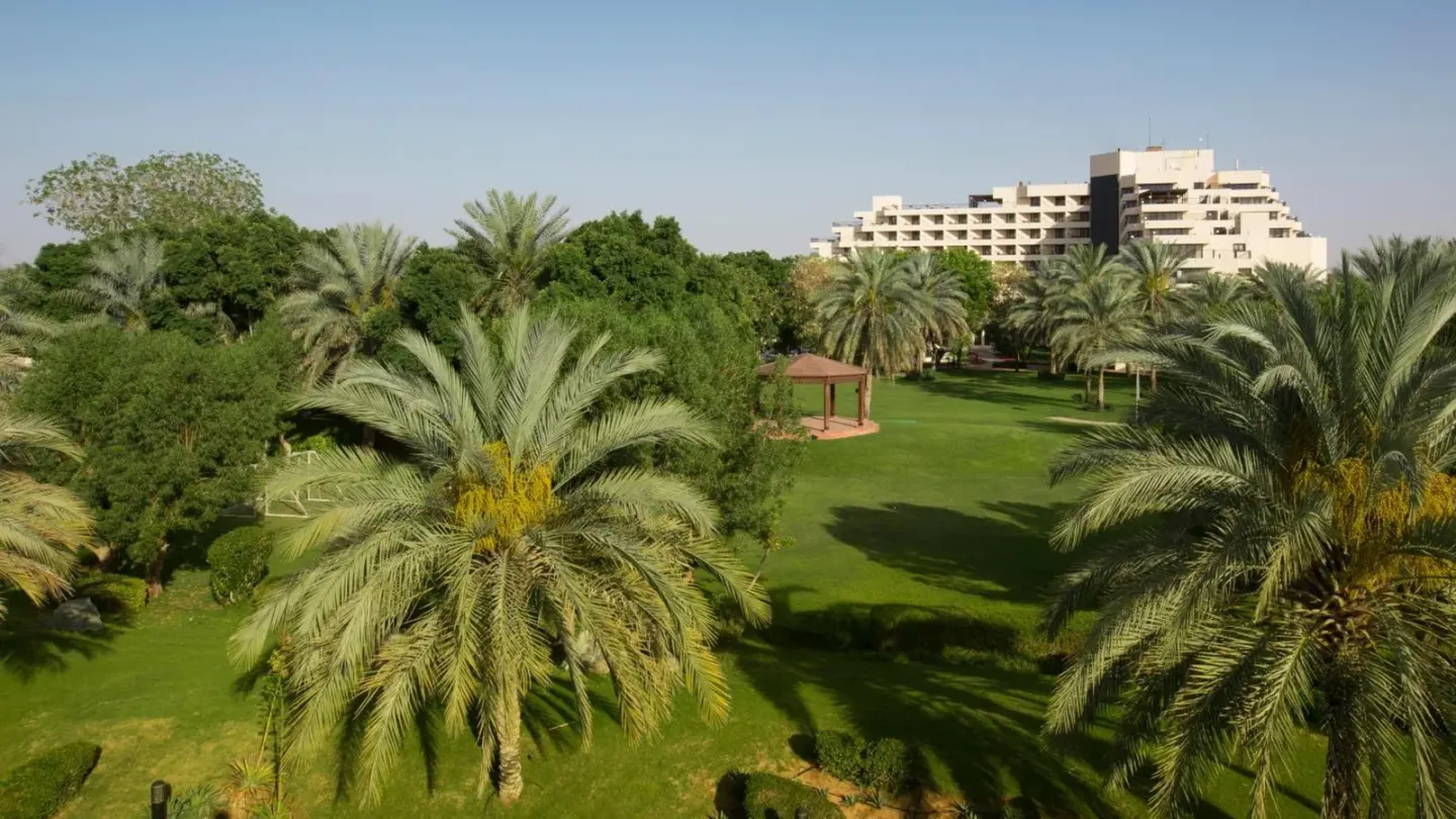 Jardins verdoyants et palmiers au Danat Al Ain Resort à Al Ain avec le bâtiment de l’hôtel au loin.