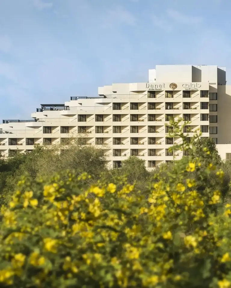 Vue extérieure de Danat Al Ain Resort à Al Ain encadrée par des fleurs jaunes et de la verdure.