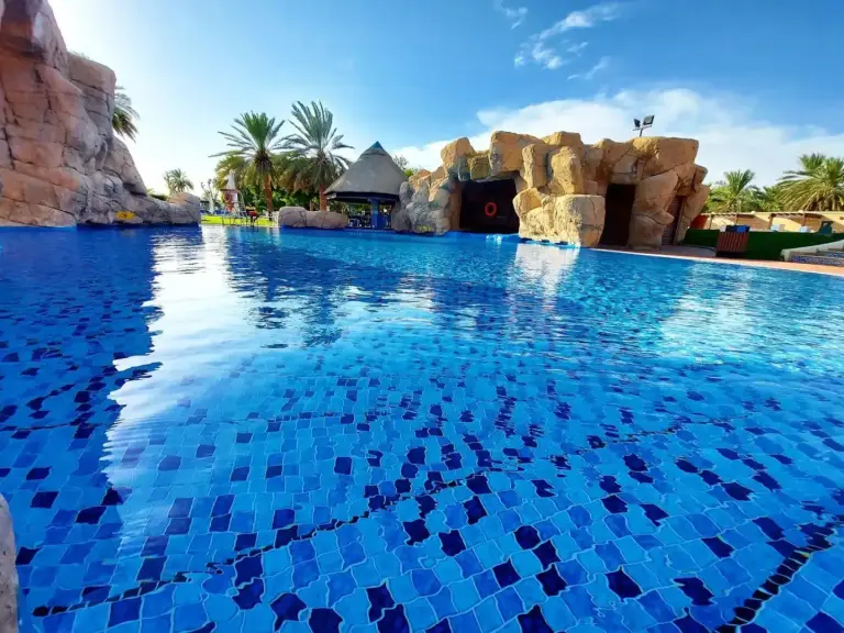 Grande piscine bleue au Danat Al Ain Resort à Al Ain avec des éléments rocheux et un aménagement paysager tropical.