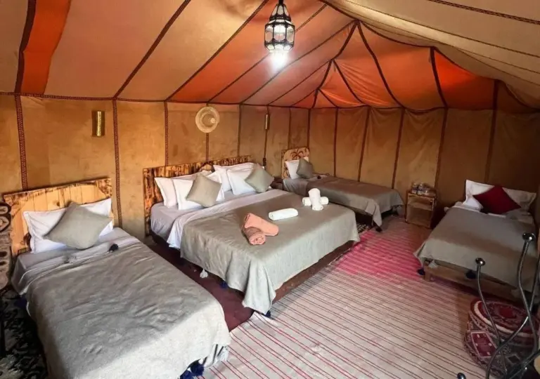 Desert Aura Luxury Camp in Merzouga family tent room with multiple beds and colorful rugs