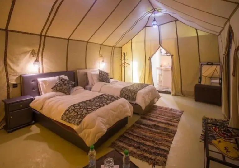 Desert Aura Luxury Camp in Merzouga twin tent room with two beds, patterned pillows, and a private bathroom entrance