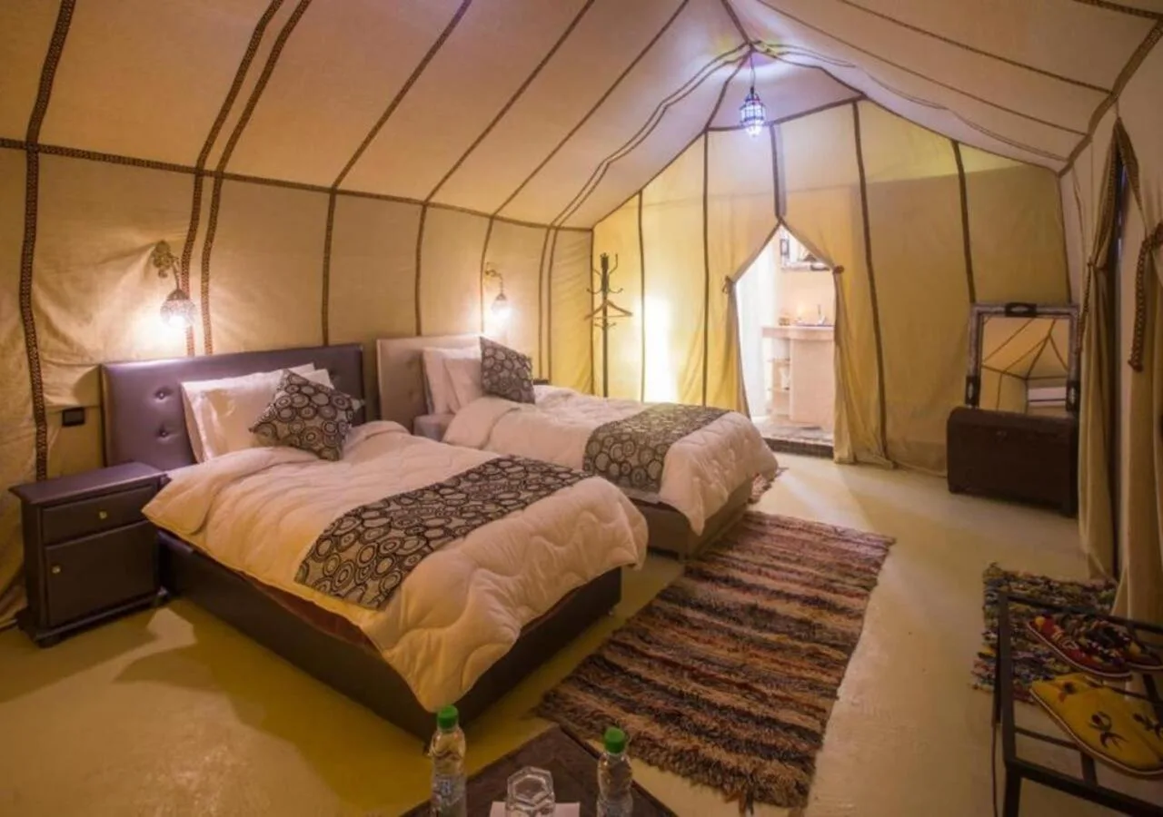 Desert Aura Luxury Camp in Merzouga twin tent room with two beds, patterned pillows, and a private bathroom entrance