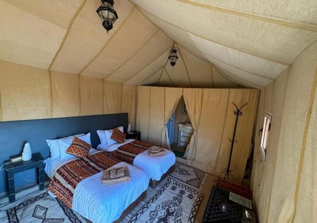 Desert Aura Luxury Camp in Merzouga twin tent room with two beds, rugs, and cream-colored canvas walls
